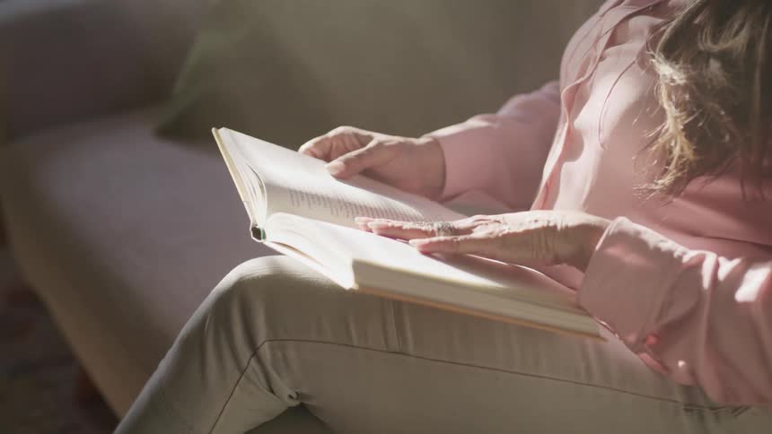 Woman sitting on couch reading a book near the sunlight