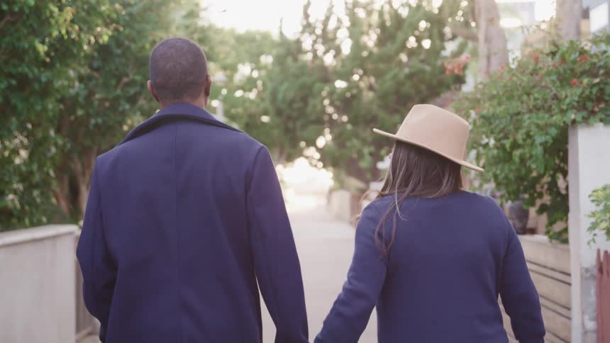 A man and woman walk along a path in a park while holding hands