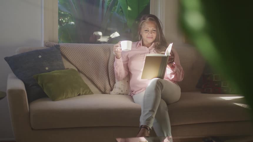 A woman is reading a book while sitting on a couch