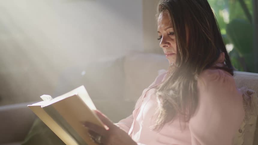 Light shines onto woman sitting reading a book as cars pass by outside the window