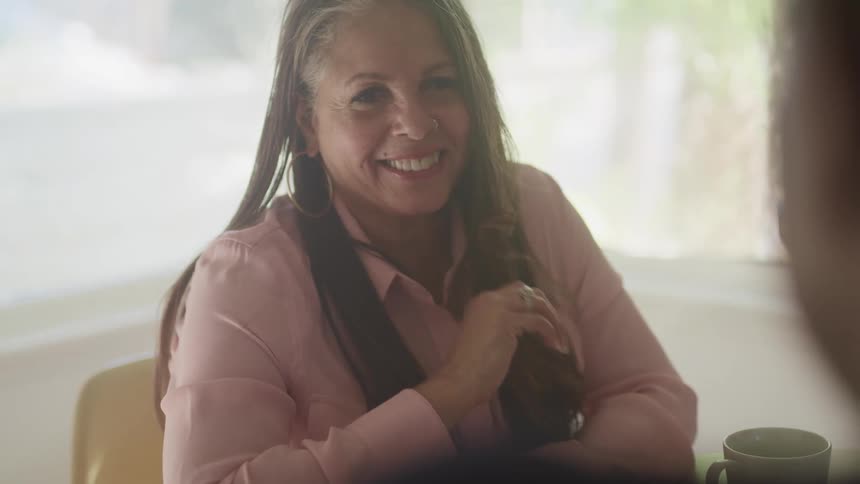 A female smiling at a male sitting at a table with a mug