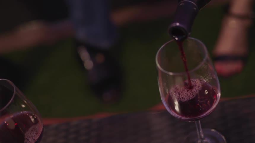 Red wine is poured into a stemmed wine glass on a table