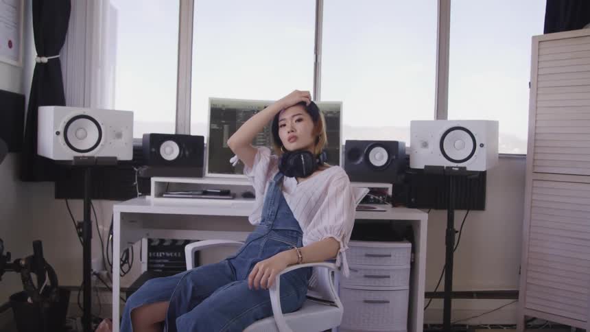 Woman wearing headphones sits in a chair in a studio in front of a computer