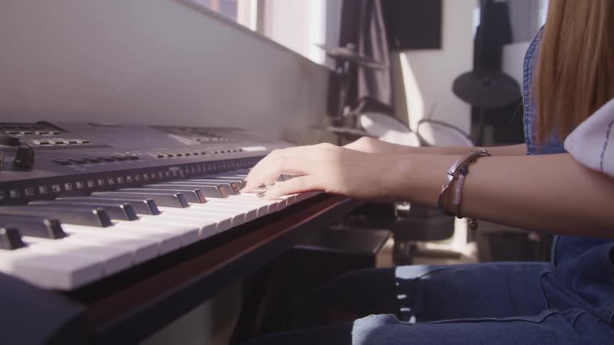 Woman with brown hair plays a digital piano in a room