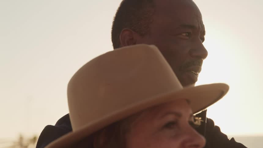 A man and woman stand outside together and the man points at something in the distance