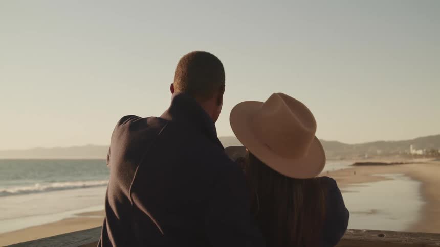 A man puts his arm around his wife as they stand on a balcony above the beach