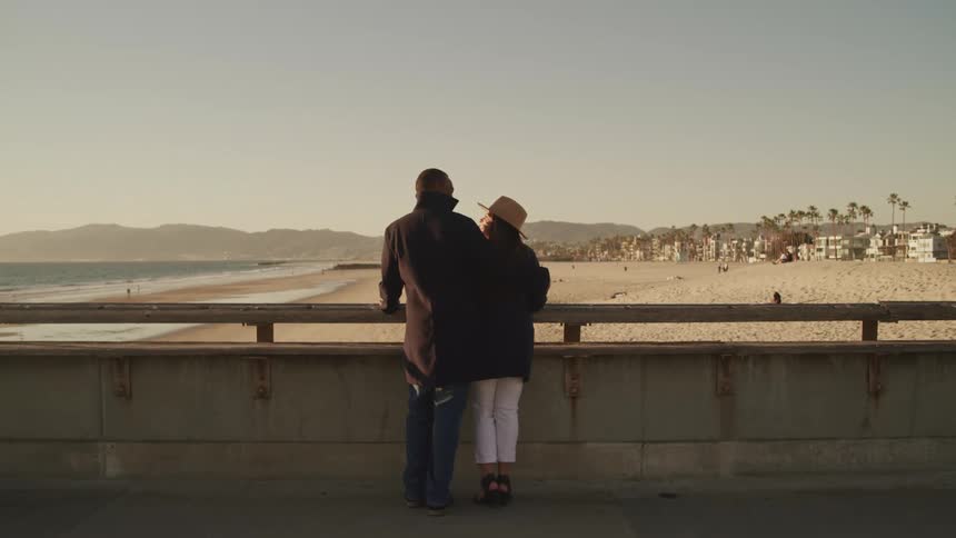 Couple stand close together at rail looking out toward beach