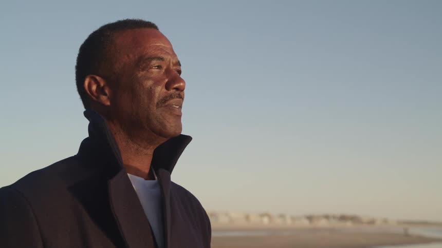 A man standing on the beach looking towards the water