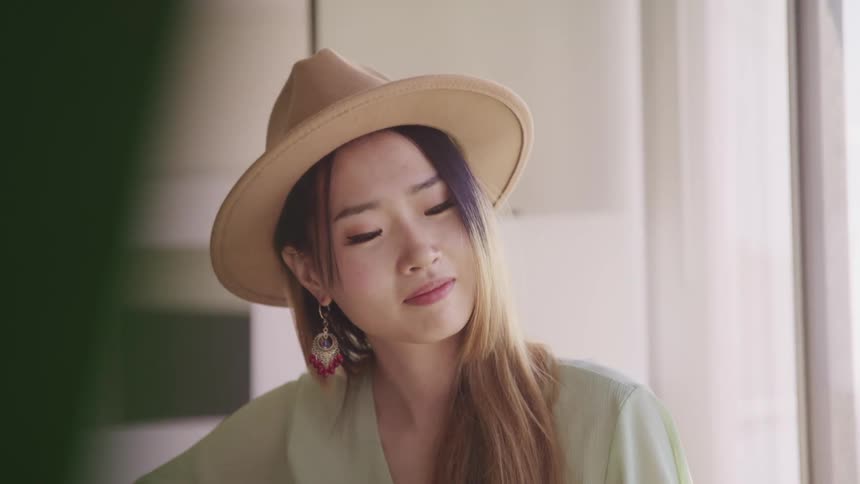 A woman with a hat sitting next to a window playing a guitar