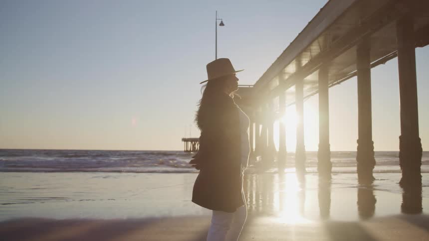 A woman looks down the beach as she stands by a pier