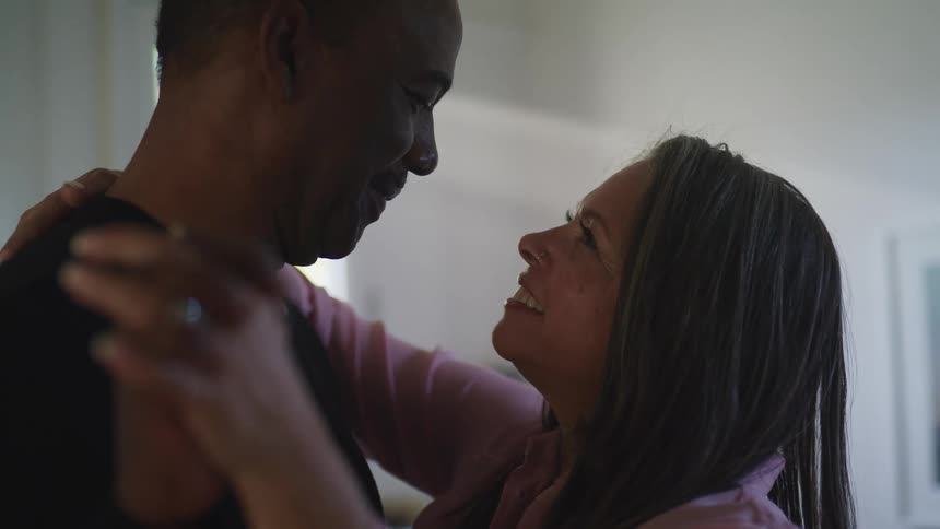 Black man and white woman look into each others eyes with affection and dance together in a room