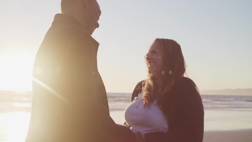 A man and woman hold hands and laugh as they stand on the beach