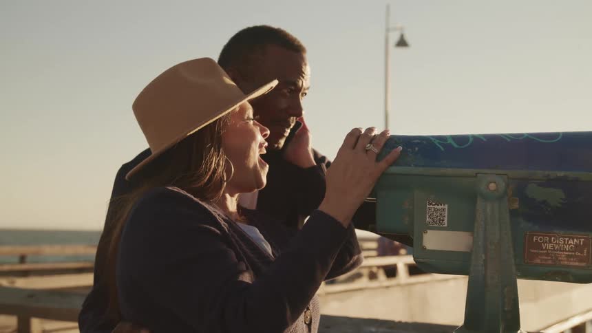 A husband and wife look through a telescope on the boardwalk