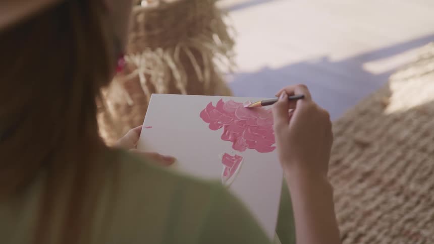 A woman brushing pink paint onto a white canvas