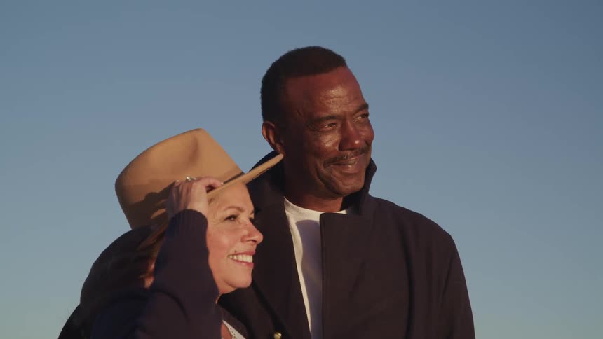 A man with his arm around a woman smiles down at her as she gazes at him
