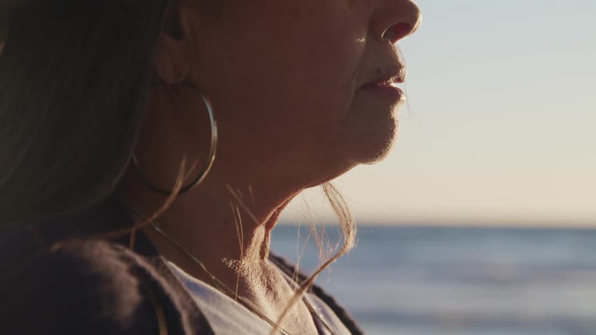 A woman with earrings standing on a beach with the ocean sky and clouds in the background