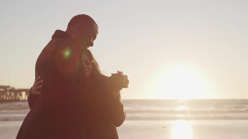 A couple holds each other close while subtly dancing on the beach as the sun sets