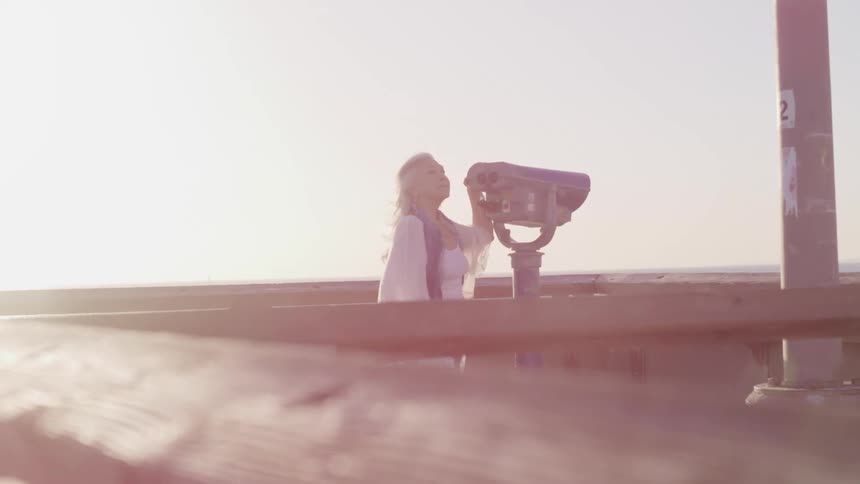 Elderly woman standing in a pier next to binoculars at sunset
