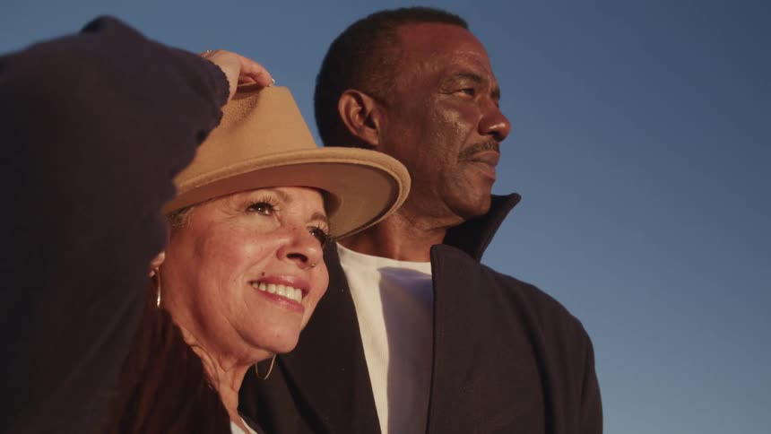 A man and woman look at something out of frame while standing outdoors on a sunny day