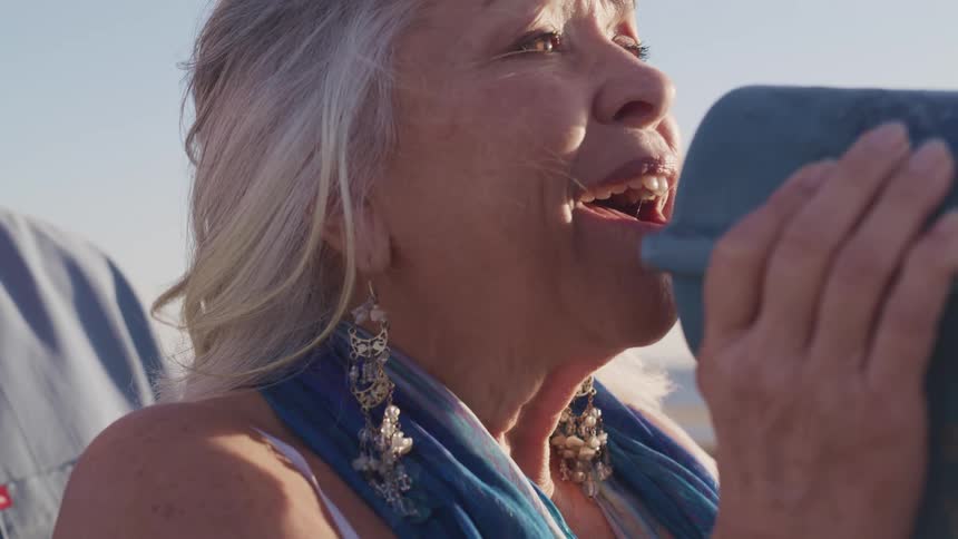 An elderly woman looks up from a telescope and smiles