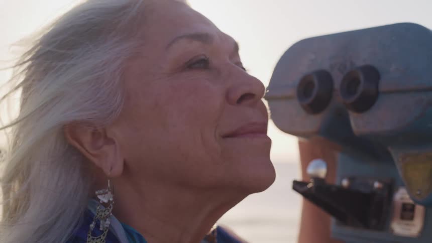 Close up of an elderly womans face next to binoculars in the beach at sunset