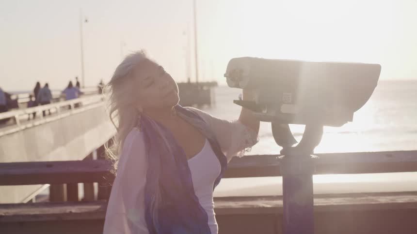 A woman standing on a pier next to a telescope and people walking