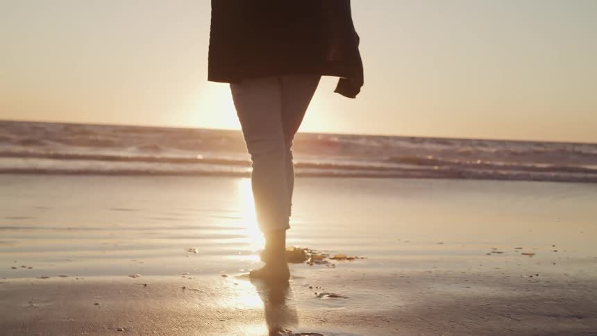 A person walks on the beach at sunset