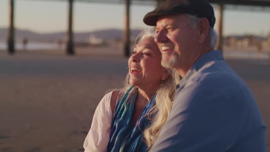An elderly couple sitting on a beach smiling