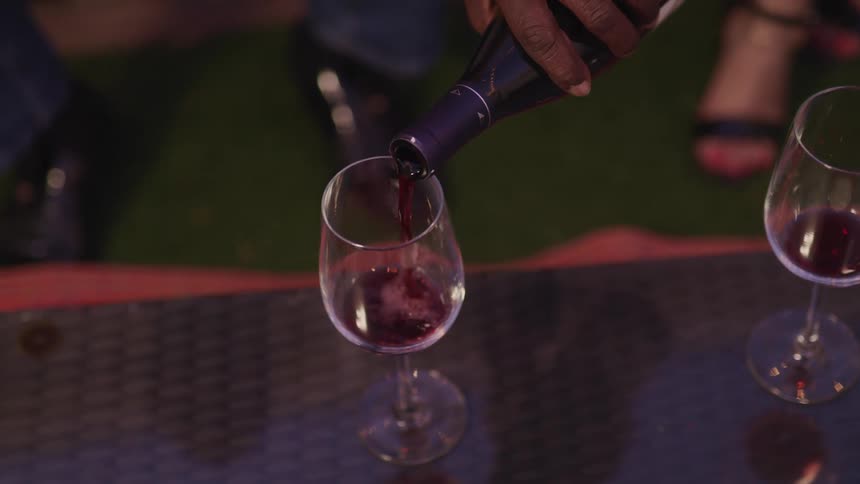 A man pours red wine into a stemmed wine glass