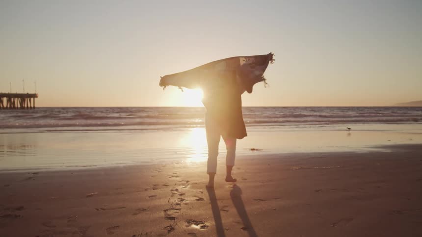 A woman runs and spins around on the beach