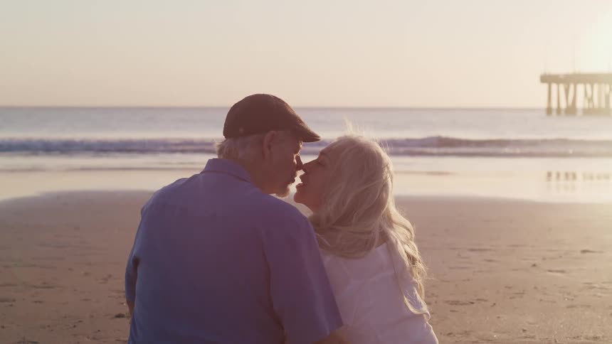 Husband and wife are kissing at the beach while the sun is setting