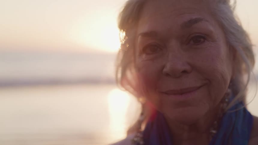 An elderly woman standing and smiling near a river