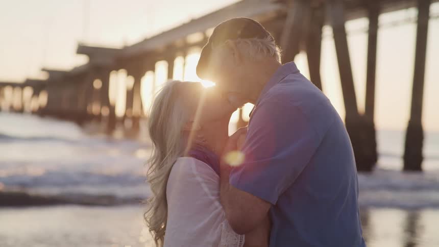 A man and woman kissing on the beach as waves roll in