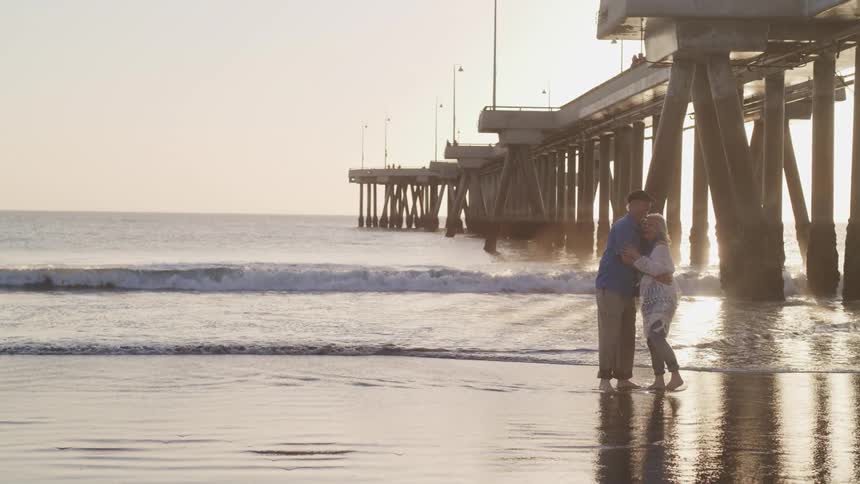 A man and woman standing on a beach next to a pier with the sky in the background