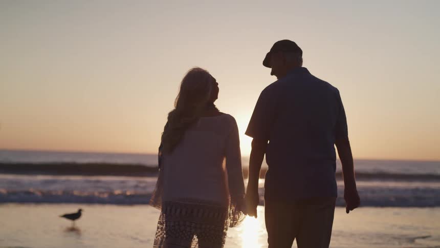 A man and woman walking down the beach holding hands
