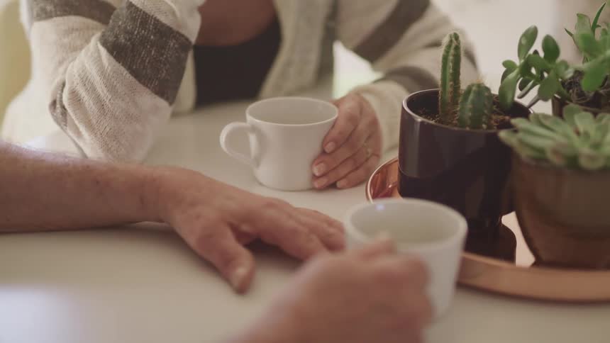 Man and woman sit at a table and hold cups while talking to each other