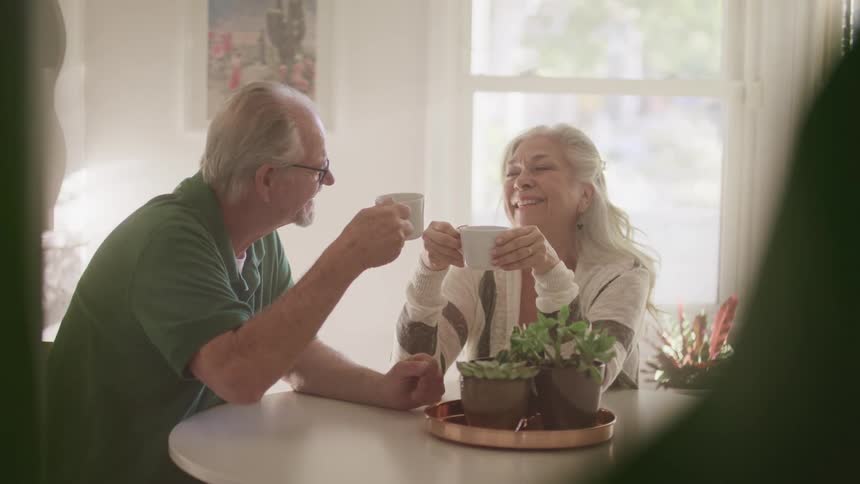 An elderly couple sitting at a table drinking from mugs