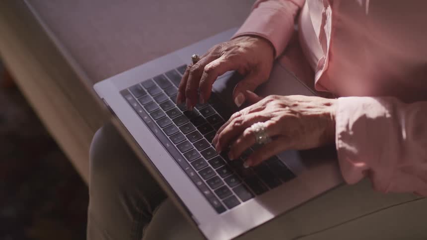 An elderly woman is typing on a laptop