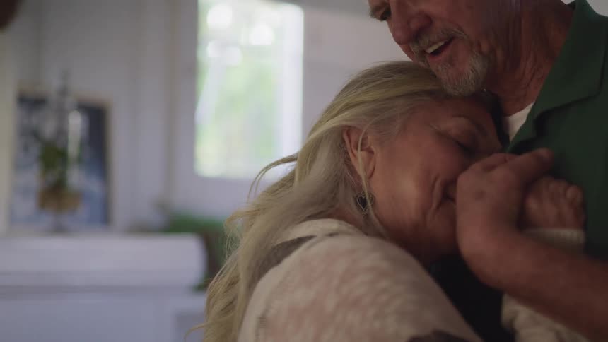Sentimental elderly couple holds hands and dances together in a room