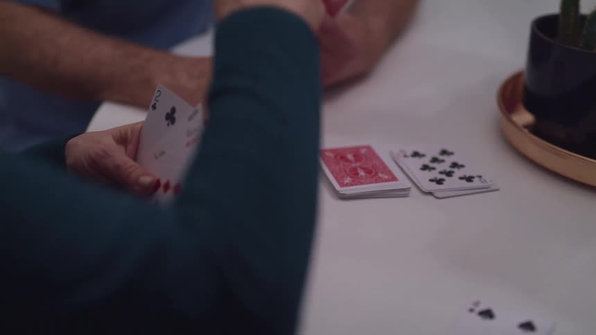 Elderly man and woman sitting at a table play cards