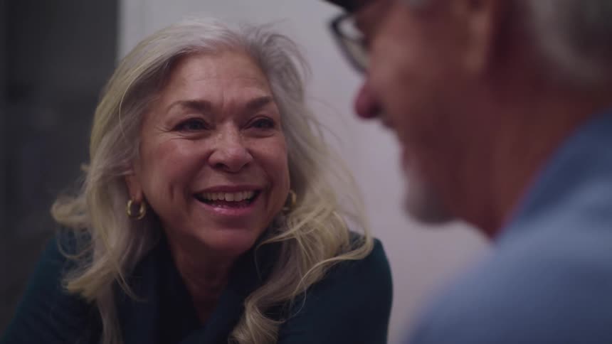 Elderly woman with grey hair and earrings looks at elderly man with a blue shirt and glasses with affection
