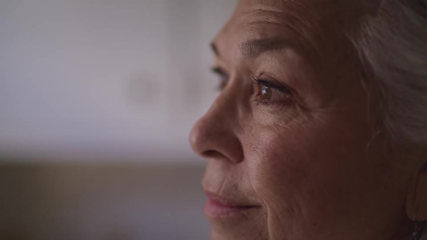 Side view of an elderly woman with grey hair smiling and looking into space