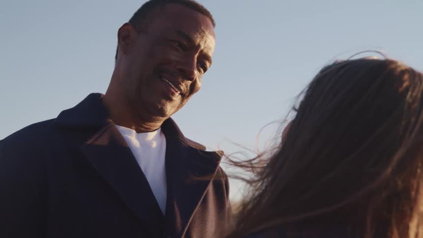 An aging black man speaks to a younger woman as they stand together outdoors on a sunny day