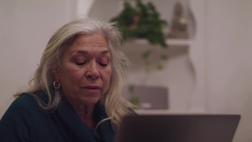 Senior woman talking on a laptop video call in the living room at home