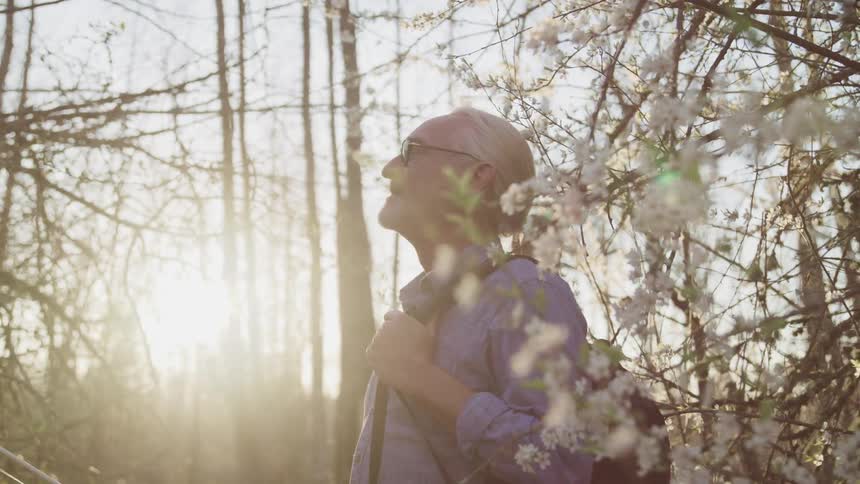 Elderly man wearing a backpack stands in the forest at sunset