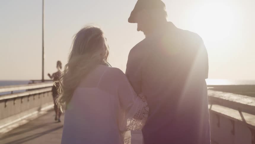 An older woman and man lock arms as they walk an ocean pier