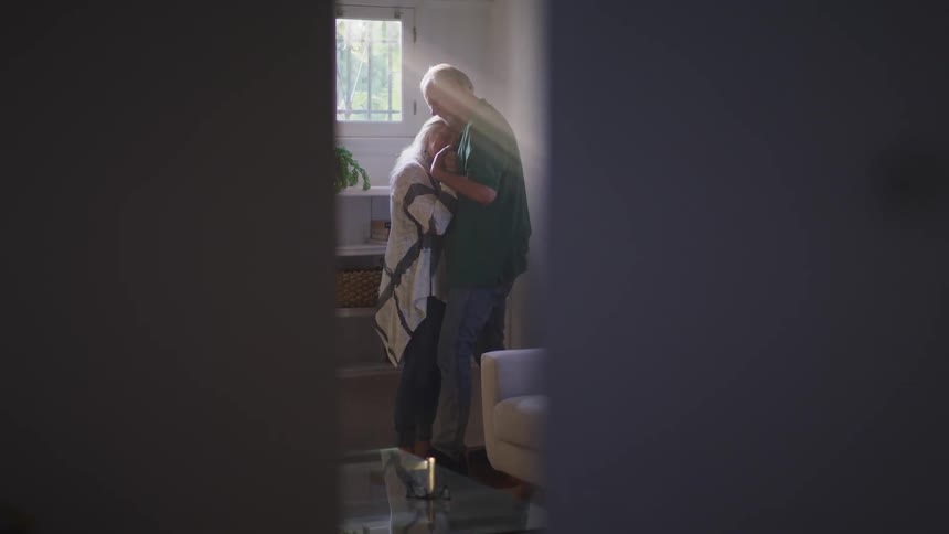 Elderly couple dances slowly in the living room while sunlight filters through the window