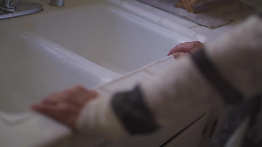A person is reclined on the kitchen counter top next to the sink at home