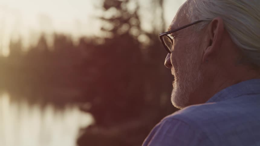 An elderly man looks out at a lake