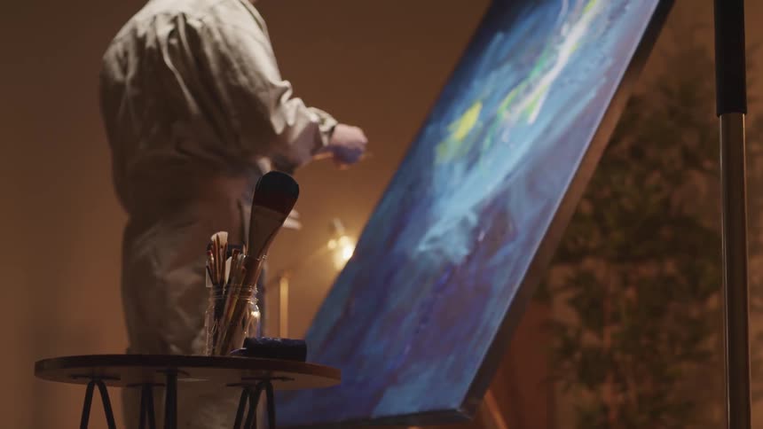 An artist brushes paint onto a large canvas indoors